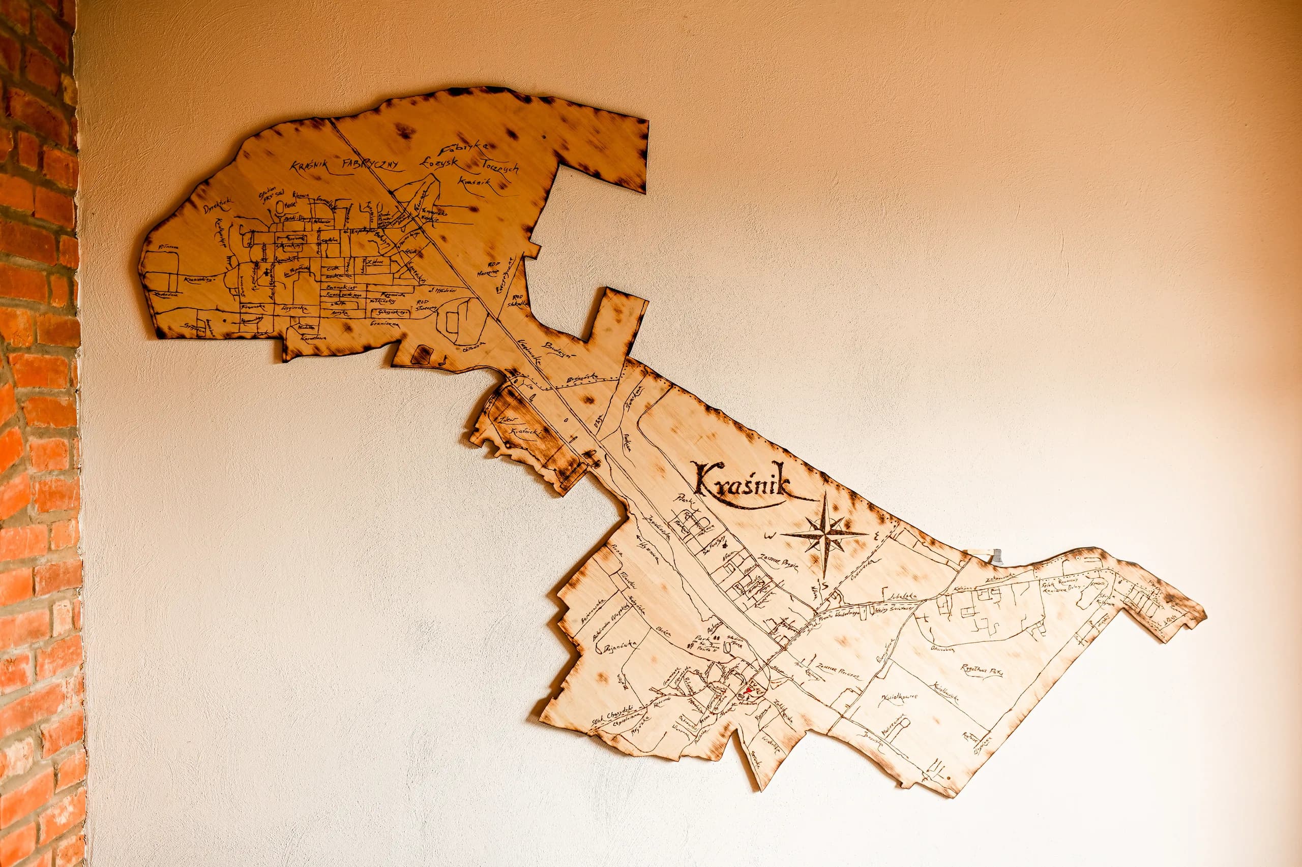 Drewniana mapa Kraśnika na jasnej ścianie obok ceglanego fragmentu wnętrza